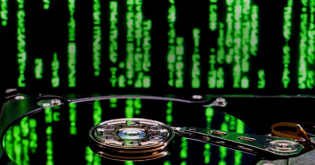 Close-up of an opened high-capacity hard drive's platter and read-write actuator, overlaid with green digital code, illustrating the growth in hard drive capacity toward 100TB.