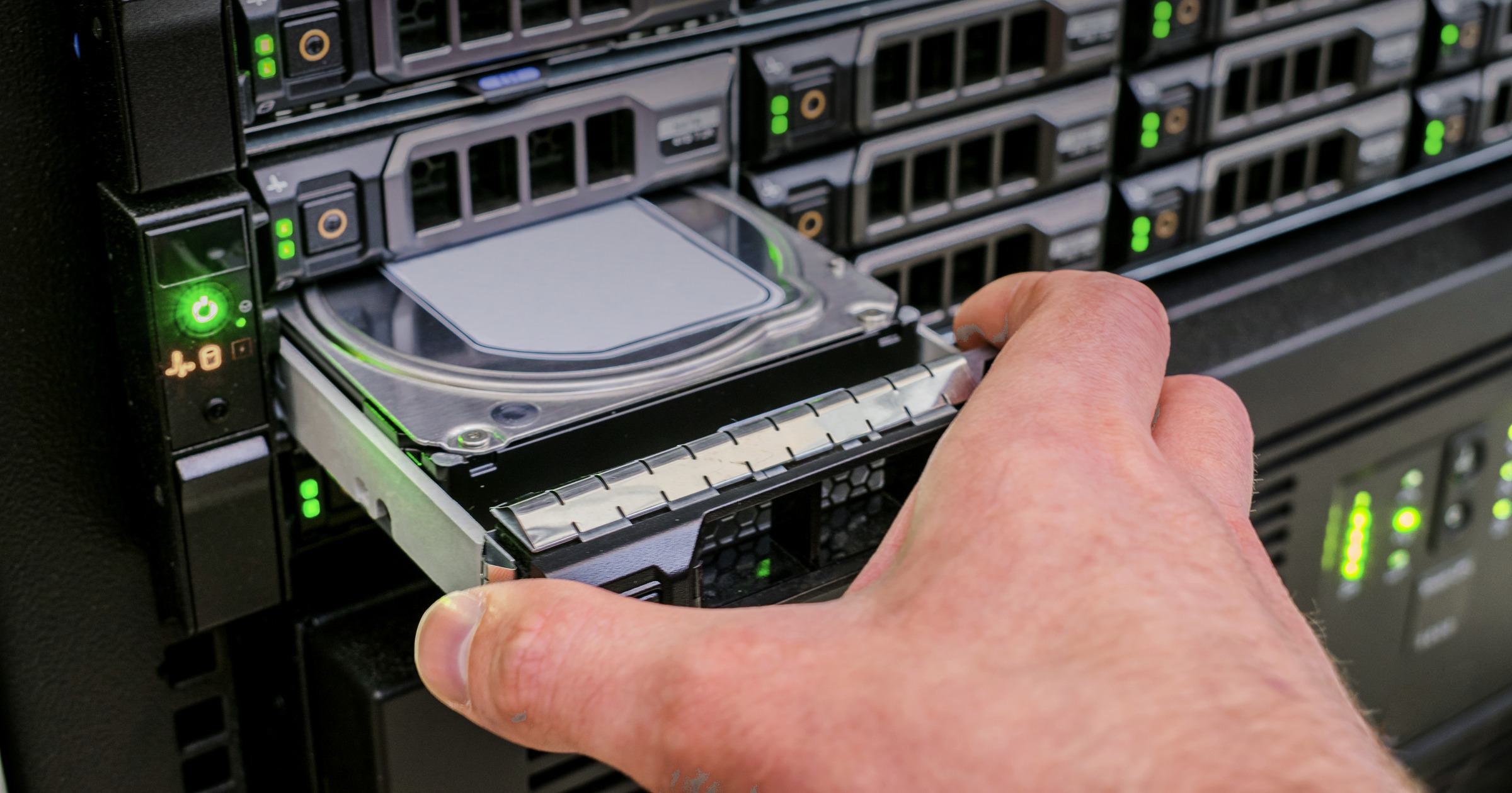 Technician hot-swapping a hard drive into a populated enterprise storage array with status LEDs lit.